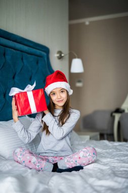 Noel Baba'nın şapka deneyin ne hediye kutusunda beyaz yatakta otururken olduğunu anlamak için çekici çocuk kız