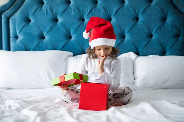Sevimli küçük kız ise bir hediye kutusu açma ve onun yatağında onun odasına evde otururken gülümseyen şaşırır — Stok fotoğraf