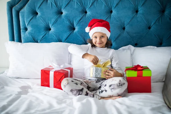 Ziemlich lustige Kind Mädchen öffnet Geschenke von Weihnachtsmann im Bett am Weihnachtsmorgen — Stockfoto