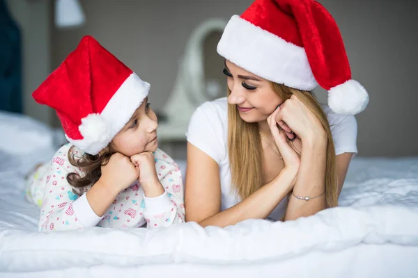 Ευτυχισμένη οικογένεια στην κρεβατοκάμαρα. Μητέρα και παιδί σε εσωτερικούς χώρους σε santa καπέλο στο κρεβάτι. Άνθρωποι έχοντας διασκέδαση στο σπίτι. Έννοια διακοπές Χειμώνας Χριστούγεννα Χριστούγεννα Πρωτοχρονιά — Φωτογραφία Αρχείου