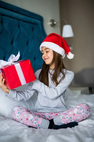 Noel Baba'nın şapkalı Noel sabahı yatakta otururken ona hediye kutusu seyir çekici çocuk kız — Stok fotoğraf
