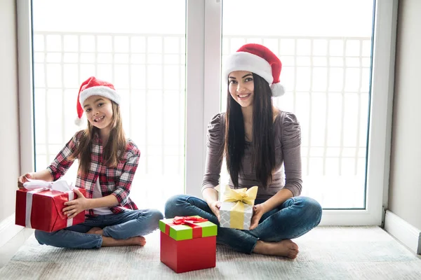 Genç gülümseyen anne ile kızı çok Noel sabahı yerde otururken kameraya bakarak yeteneğin ile Noel Baba'nın şapkalı — Stok fotoğraf