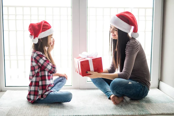 Mor ger gåva sin förvåning till lycklig dotter med clossed ögon sitter på golvet på juldagsmorgonen — Stockfoto