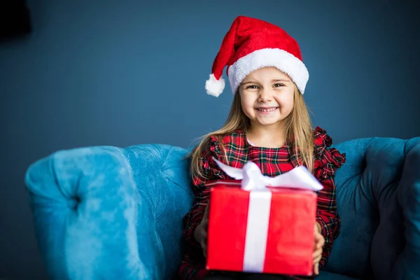 Noel hediye oturan sandalyede evde gülümseyen elbise ve santa şapka giyen güzellik güzel kız — Stok fotoğraf