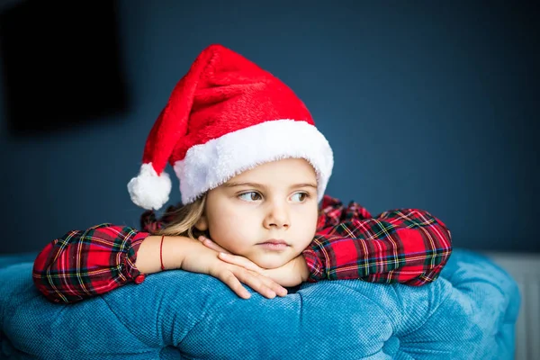 Evde pencereden bakarak Noel Baba için bekleyen Noel Baba şapkası, oldukça küçük kız portresi. Noel arifesi. — Stok fotoğraf
