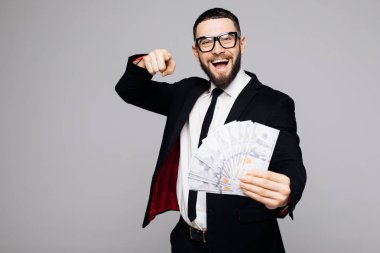 Takım elbise ve sana gri arka plan üzerinde izole para banknot para grup ile parmakla gözlük gülümseyen bir başarılı adam portresi