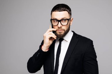 Cep telefonu gri arka plan üzerinde siyah uymak ciddi genç çekici adam portresi