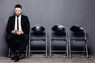 Görüşme için hazır. Yakışıklı adam telefon tutarak resmi kıyafeti içinde ve sandalyeye bekleme odasında otururken kullanabilirsiniz