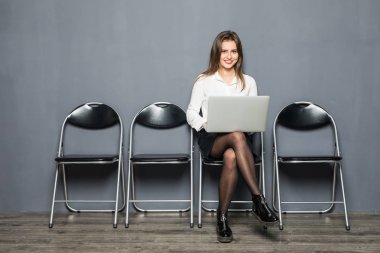 mobil dizüstü bilgisayar kullanan ahşap zemin sandalyede oturan işçisi kadın ofis gülümseyen genç gri salonunda röportaj toplantı dosyasını hazırlama