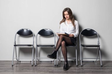 Kağıt tutan ve uzak gri bir arka plana dayanır sandalyede otururken arıyorum genç iş kadını