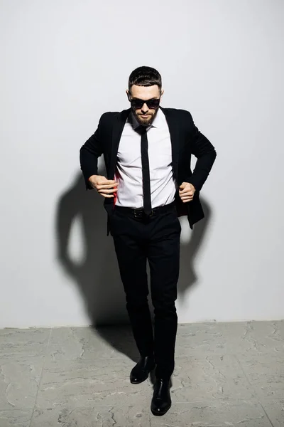 Retrato de un hombre guapo y elegante en traje y corbata posando mientras está de pie y mirando hacia otro lado sobre fondo gris — Foto de Stock