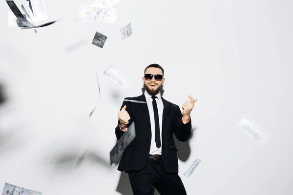 Bonito homem de fato e óculos de sol apontado para cima em dinheiro líquido em fundo branco. Empresário em pé à chuva de dinheiro . — Fotografia de Stock