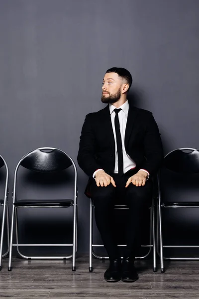 Ung snygg man med skägg förbereder sig för intervjun klädd i kostym, sitter på stol, väntar i office hall — Stockfoto