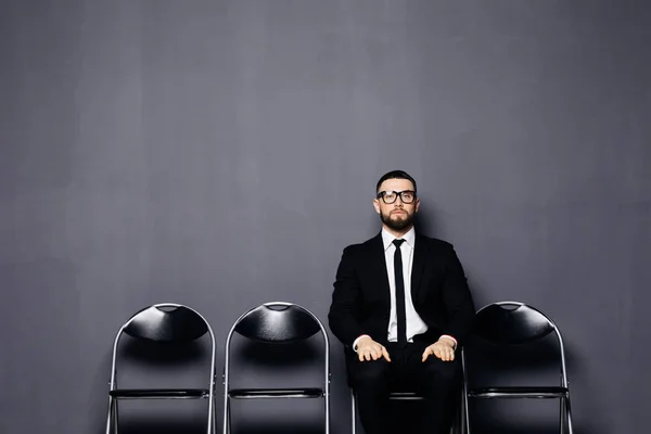 Sakallı genç şık adam bir takım elbise giymiş, sandalyede oturan, ofis salonunda bekleyen görüşme için hazırlanıyor — Stok fotoğraf