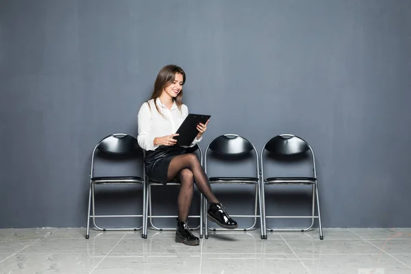 Jovem mulher bonita à espera de entrevista de emprego com blanck em mãos sobre fundo cinza — Fotografia de Stock