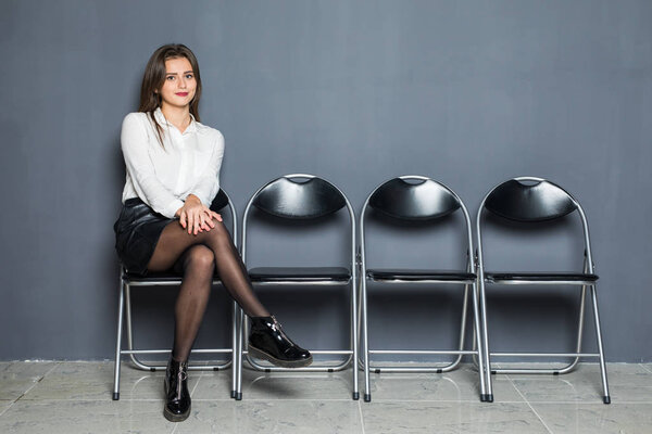 confident businesswoman sitting on chair and waiting for interview on gray background