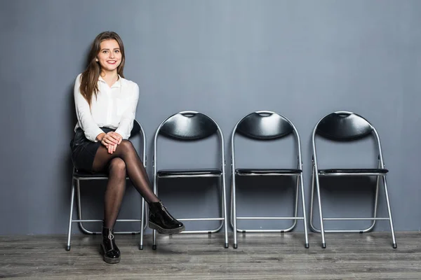 Mulher de negócios confiante sentado na cadeira e à espera de entrevista em fundo cinza — Fotografia de Stock