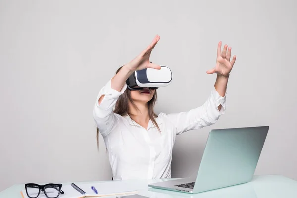 Mujer con gafas VR. Mujer joven y segura con auriculares de realidad virtual apuntando en el aire mientras está sentada en su lugar de trabajo en la oficina — Foto de Stock