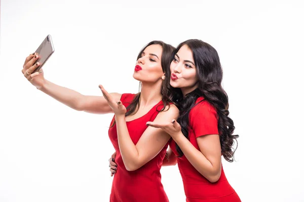 Duas jovens mulheres de beleza vestindo vestido vermelho tomando selfie no fundo branco — Fotografia de Stock