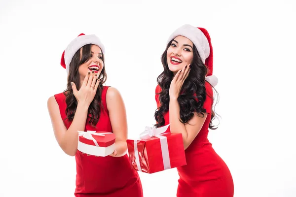 Retrato de dos hermosas mujeres felices en sombreros de navidad mostrando cajas de regalo aisladas en el campo de juego —  Fotos de Stock