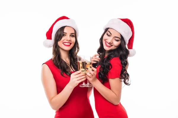 Retrato de dos niñas sonrientes felices en vestidos rojos y sombreros de santa celebración de copas con champán mientras brindan y mirando a la cámara sobre fondo blanco —  Fotos de Stock
