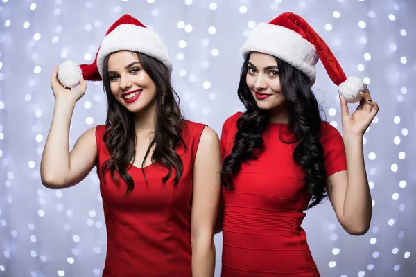 Retrato de dos mujeres en sombreros de santa y vestido rojo sobre fondo claro bokeh. Vacaciones de invierno Navidad y Año Nuevo concepto —  Fotos de Stock