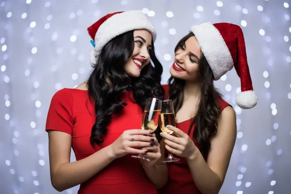 Noel Baba şapkaları ve kırmızı elbise alkış ve İçecek şampanya bokeh ışık arka plan üzerinde iki kadın portresi. Kış tatil Noel ve yeni yıl kavramı — Stok fotoğraf