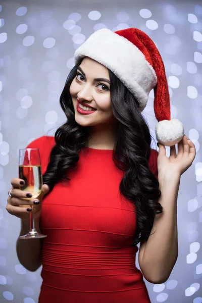 Porträtt av kvinna i santa hatt och röd klänning med champagne på bokeh ljus bakgrund. Vinter semester jul och nyår koncept — Stockfoto