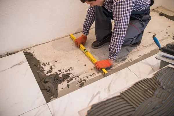 Home improvement, renovation - handyman laying ceramic tile with level