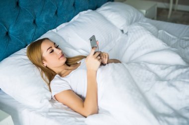 Sabah uyanma zaman yatağa akıllı telefon kullanan genç güzel kadın
