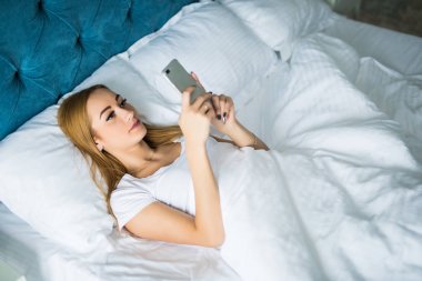 Sabah uyanma zaman yatağa akıllı telefon kullanan genç güzel kadın
