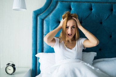 Genç kadın bir baş ağrısı ile sabah uyku modundan çıkarma sonra yatağa evde oturuyor. Acı acı ve yaralanma kavramı.