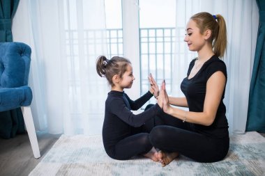 Güzel genç kadın ve büyüleyici küçük kızı yoga birlikte evde yüz yüze yaparken gülüyorsun