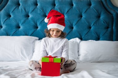 Noel mutlu oldukça küçük bir çocukla santa şapka heyecanlı hediye yatakta açarken sunar