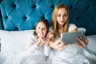 Anne ve kızı yatakta yatarken ve smartphone ile kendi kendine portre çekici. Yatak Odası, küçük bir kız ile selfie alarak kadın.