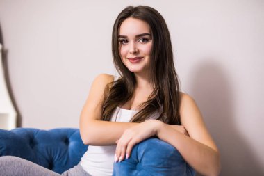 Kanepe sandalye kameraya bakarak mutlu gülümseyen içinde rahat oturan rahatlatıcı kadın.