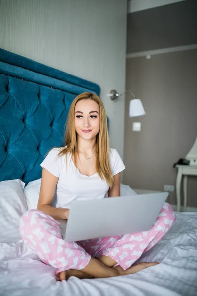 Женщина в постели с ноутбуком на ногах дома — стоковое фото