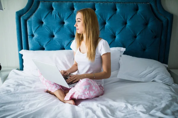 Женщина в постели с ноутбуком на ногах дома — стоковое фото