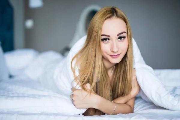 Belleza joven acostada debajo de un edredón en un dormitorio —  Fotos de Stock