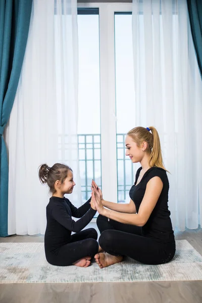 美丽的年轻女子和她迷人的小女儿在家里一起做瑜伽时，脸上挂着笑容 — 图库照片