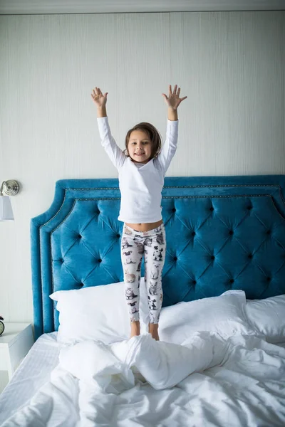 Милая маленькая девочка прыгает на белой кровати дома — стоковое фото