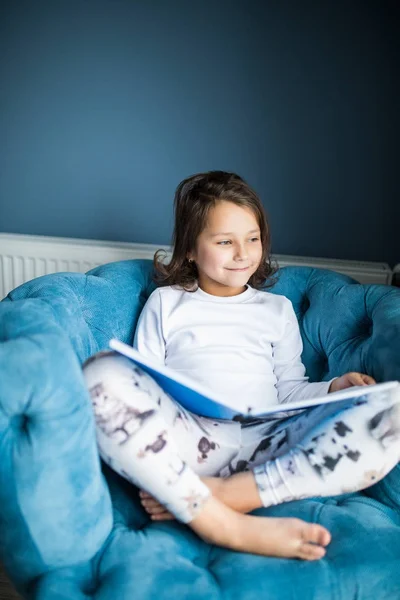 Забавная счастливая девочка читает книгу и играет в постели. Дети играют дома. Белая детская. Ребенок в солнечной спальне. Дети читают и учатся. Интерьер для малыша и малыша . — стоковое фото