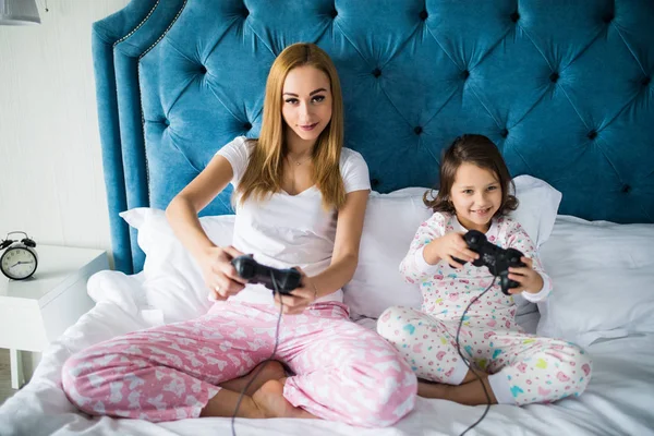 Madre e hija pequeña juegan videojuegos de consola en la cama en casa —  Fotos de Stock