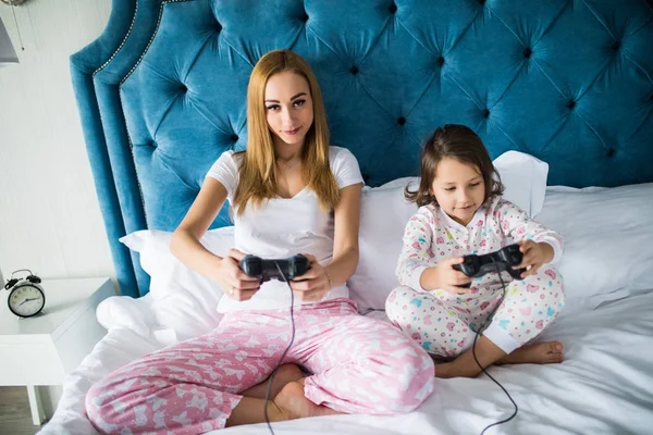 Madre e hija pequeña juegan videojuegos de consola en la cama en casa —  Fotos de Stock