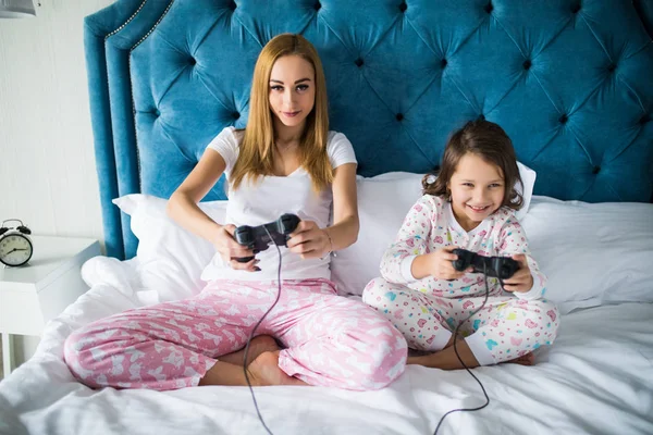 Madre e hija jugando videojuegos en la cama en casa —  Fotos de Stock