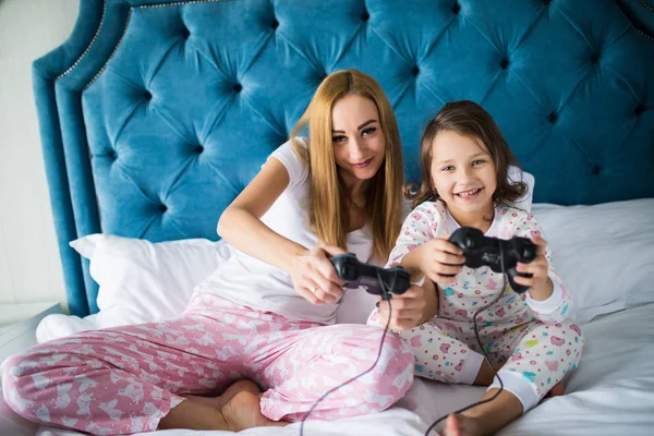 Alegre madre e hija jugando videojuegos en la cama en casa —  Fotos de Stock