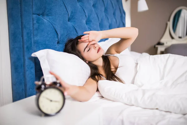 Sleepy young beauty woman stretching hand to ringing alarm to turn it off. Early wake up, not getting enough sleep, getting work concept. — Stock Photo, Image