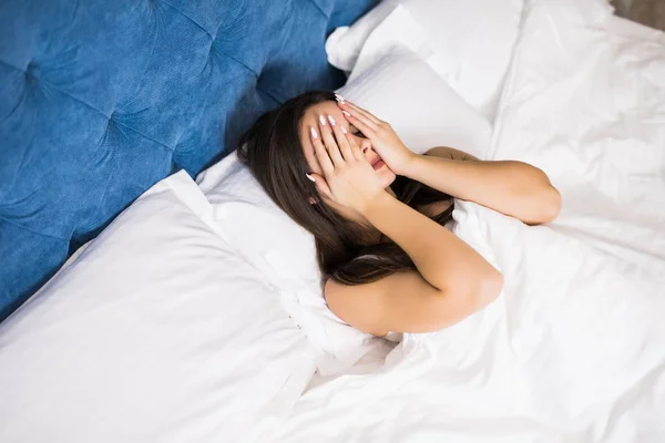 Top view of beautiful sexy young woman covering her eyes, looking at camera and smiling while lying in the bed — Stock Photo, Image