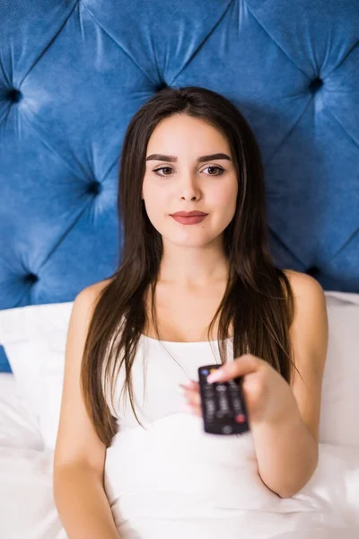 Hermosa mujer acostada en la cama, disfrutando y viendo la televisión en casa —  Fotos de Stock