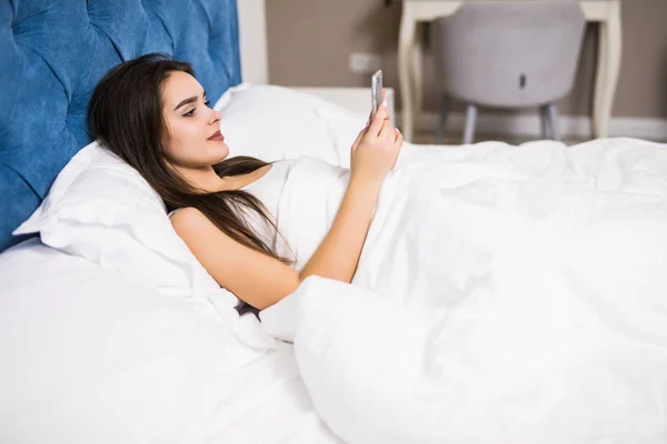 Mujer en la cama revisando aplicaciones sociales con smartphone en la mañana en casa —  Fotos de Stock